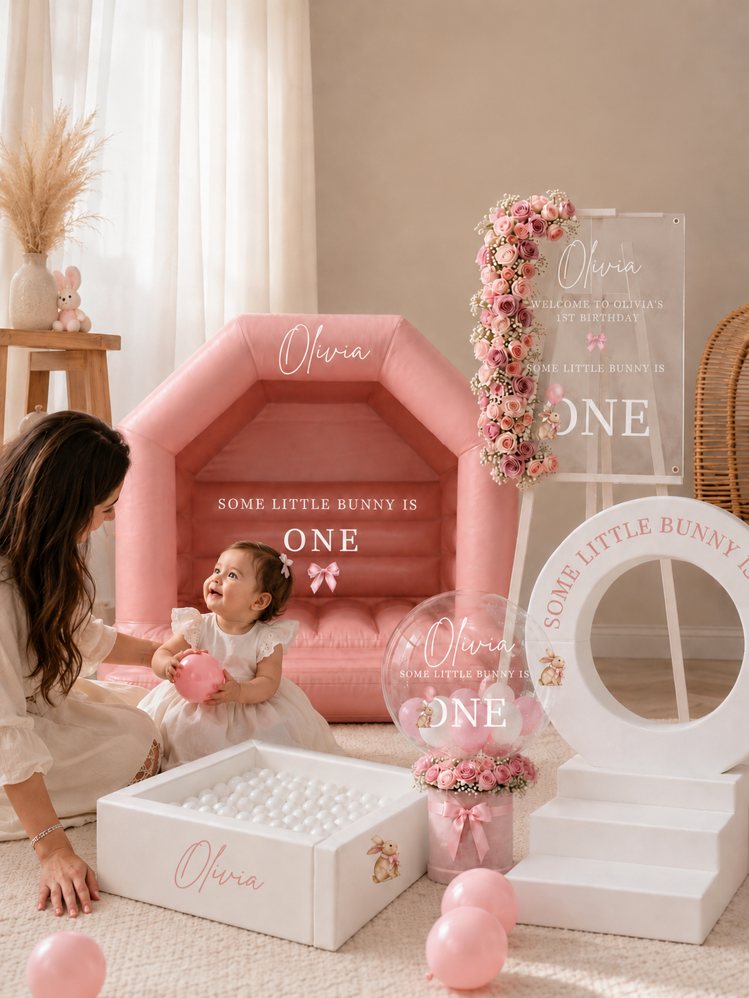 Pink personalised soft play and bouncy castle, custom acrylic birthday signage, floral number display, balloon arrangement, and matching white ball pit.