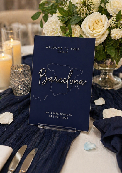 A5 navy acrylic wedding table sign with silver script “Barcelona” and subtle map