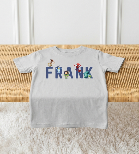 Gray t-shirt with 'FRANK' printed on it, featuring cartoon characters, on a wooden table.
