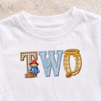 White t-shirt with 'TWO' printed on it featuring cartoon characters, on a wooden surface.