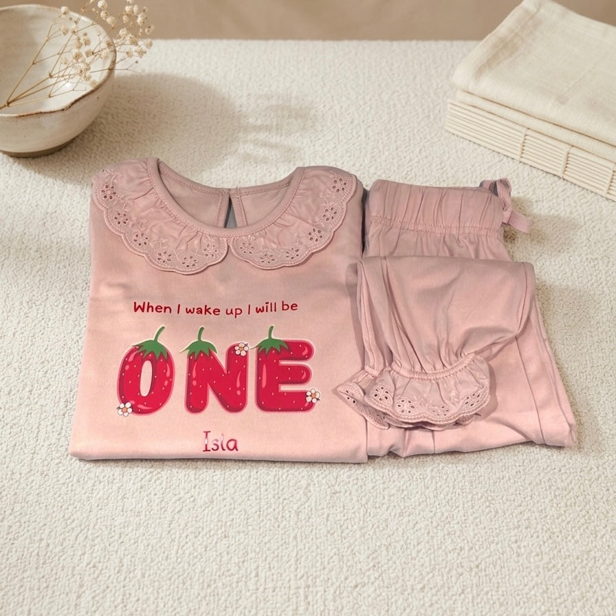 Pink children's outfit with 'When I wake up I will be ONE' text on a light surface.