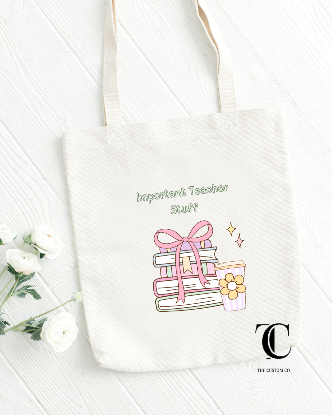 White tote bag with a design of books and a gift, text 'Important Teacher Stuff', and a logo on a light wooden background.