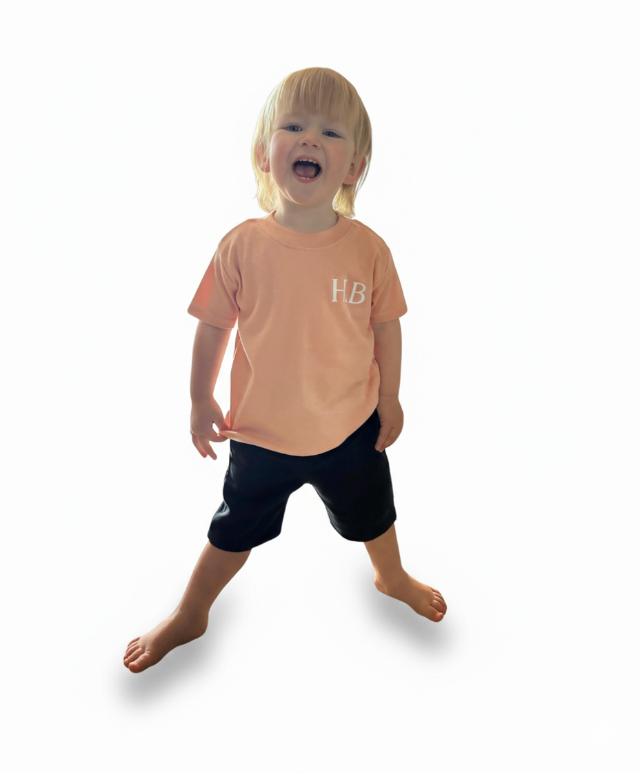 Child wearing a peach t-shirt with 'HB' logo on a white background