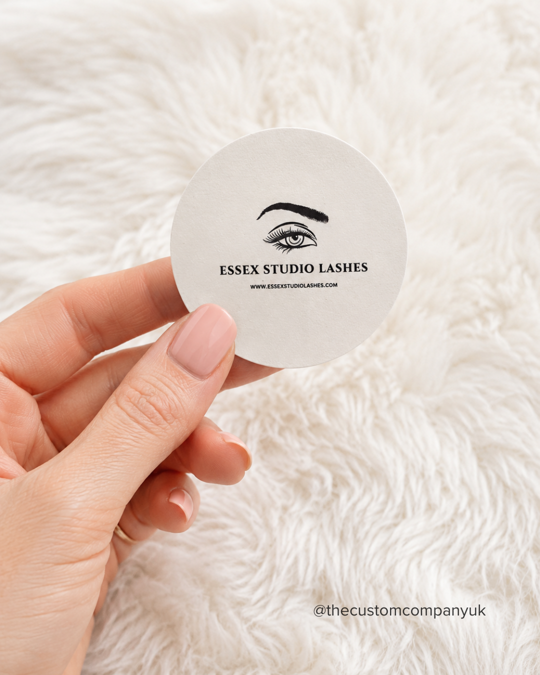 Hand holding a round 5cm sticker with 'Essex Studio Lashes' branding.