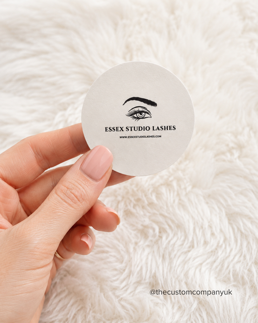 Hand holding a round 5cm sticker with 'Essex Studio Lashes' branding.