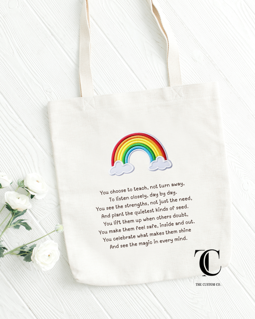 White tote bag with rainbow and cloud design, text, and logo on a white background
