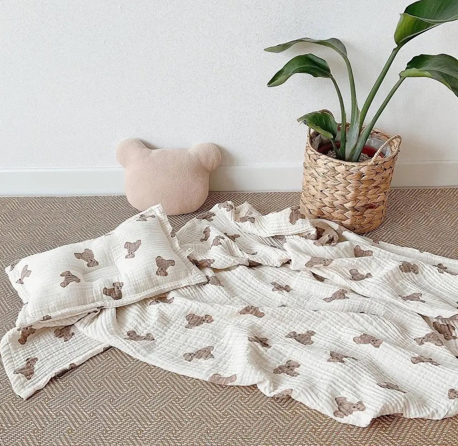Baby blanket with bear pattern, pillow, and plant on a neutral background