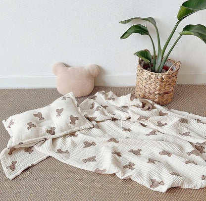 Baby blanket with bear pattern, pillow, and plant on a neutral background