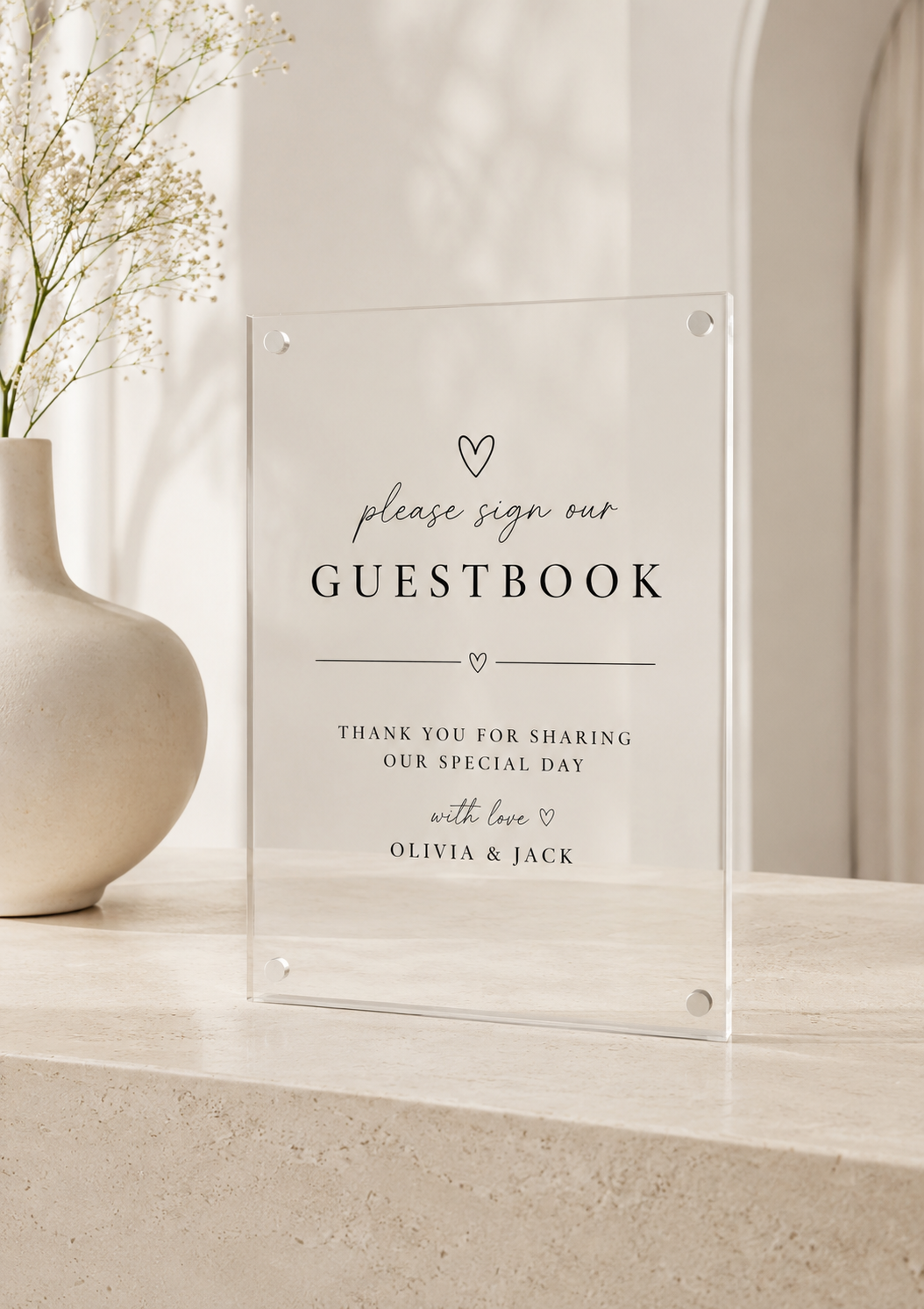 Acrylic guestbook sign on a decorative shelf with a vase and flowers.
