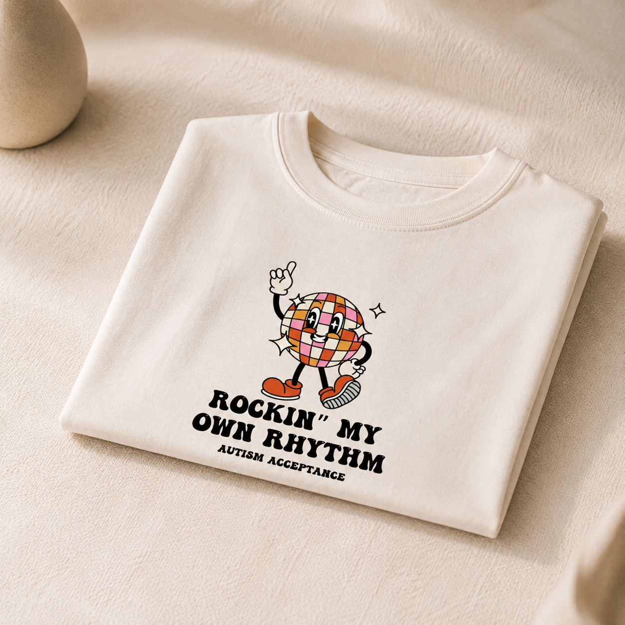 Cream children’s T shirt featuring a colourful retro disco ball character with the text “Rockin’ My Own Rhythm” and “Autism Acceptance” in black lettering.