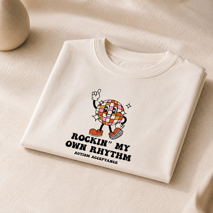 Cream children’s T shirt featuring a colourful retro disco ball character with the text “Rockin’ My Own Rhythm” and “Autism Acceptance” in black lettering.